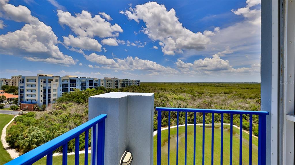 A balcony with blue railings overlooks a grassy area, dense vegetation, and distant apartment buildings — 5300 S ATLANTIC AVENUE UNIT 5601, NEW SMYRNA BEACH, FL