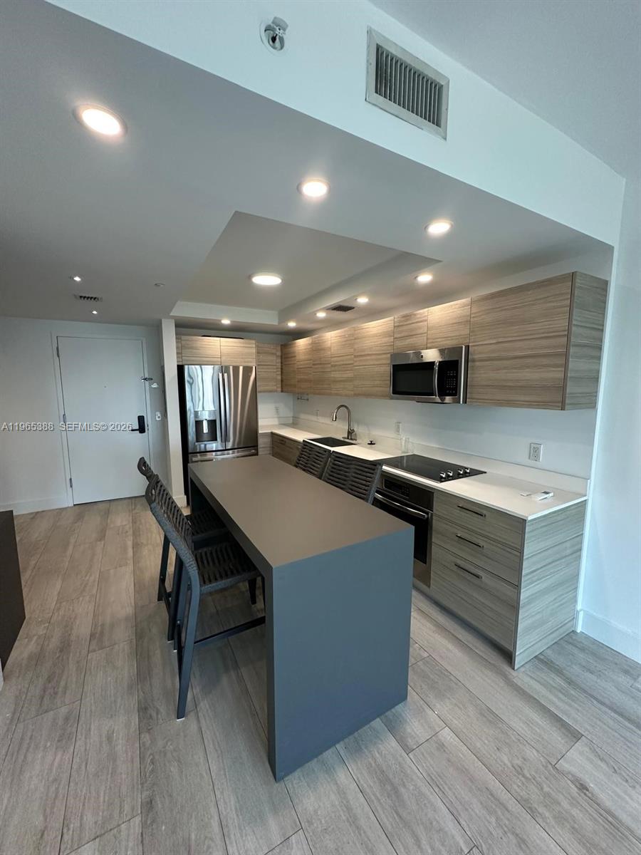 A modern kitchen features wood-grain cabinets, a gray island, and stainless steel appliances — 121 NE 34th St # 1505, Miami FL 33137, MIAMI, FL
