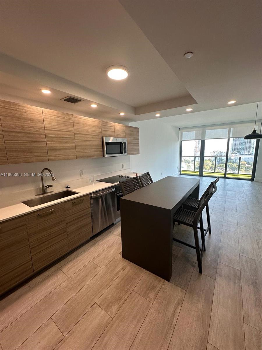 A modern kitchen features wood-grain cabinets, stainless steel appliances, and a dark island with seating — 121 NE 34th St # 1505, Miami FL 33137, MIAMI, FL