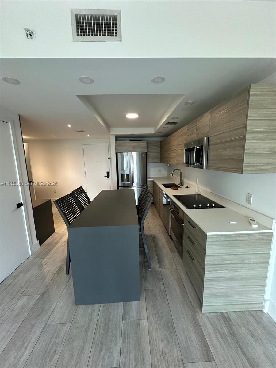 A modern kitchen features wood-grain cabinetry, a dark island, and stainless steel appliances — 121 NE 34th St # 1505, Miami FL 33137, MIAMI, FL