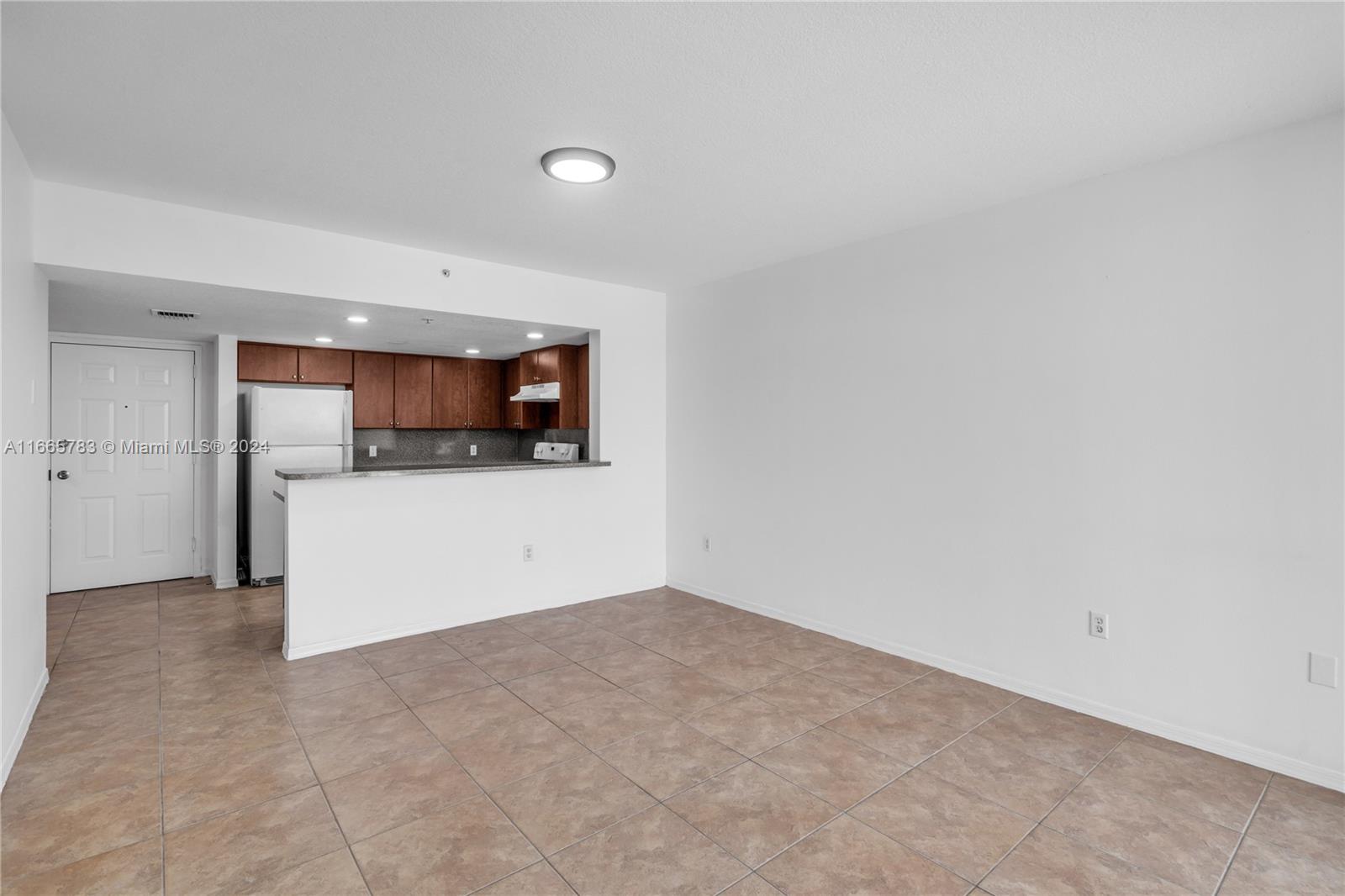 This room features light-colored tile flooring, white walls, and an open kitchen with wood cabinets — 218 NW 12th Ave # 702, Miami FL 33128, MIAMI, FL