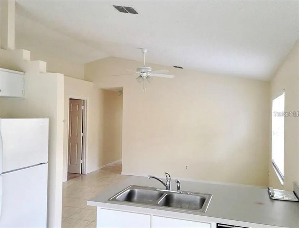 A kitchen with a double sink and white cabinets overlooks a living area with vaulted ceilings — 13706 GLASSER AVENUE, ORLANDO, FL