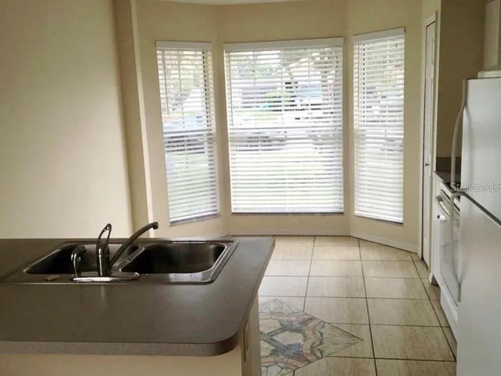 A kitchen features a double-basin sink, tile flooring, and a bay window with blinds — 13706 GLASSER AVENUE, ORLANDO, FL