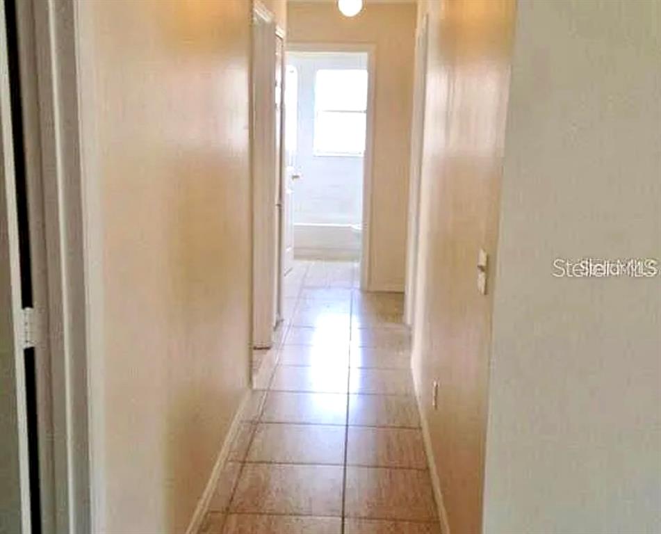 A narrow hallway with light-colored tile flooring leads toward a bathroom with a window — 13706 GLASSER AVENUE, ORLANDO, FL