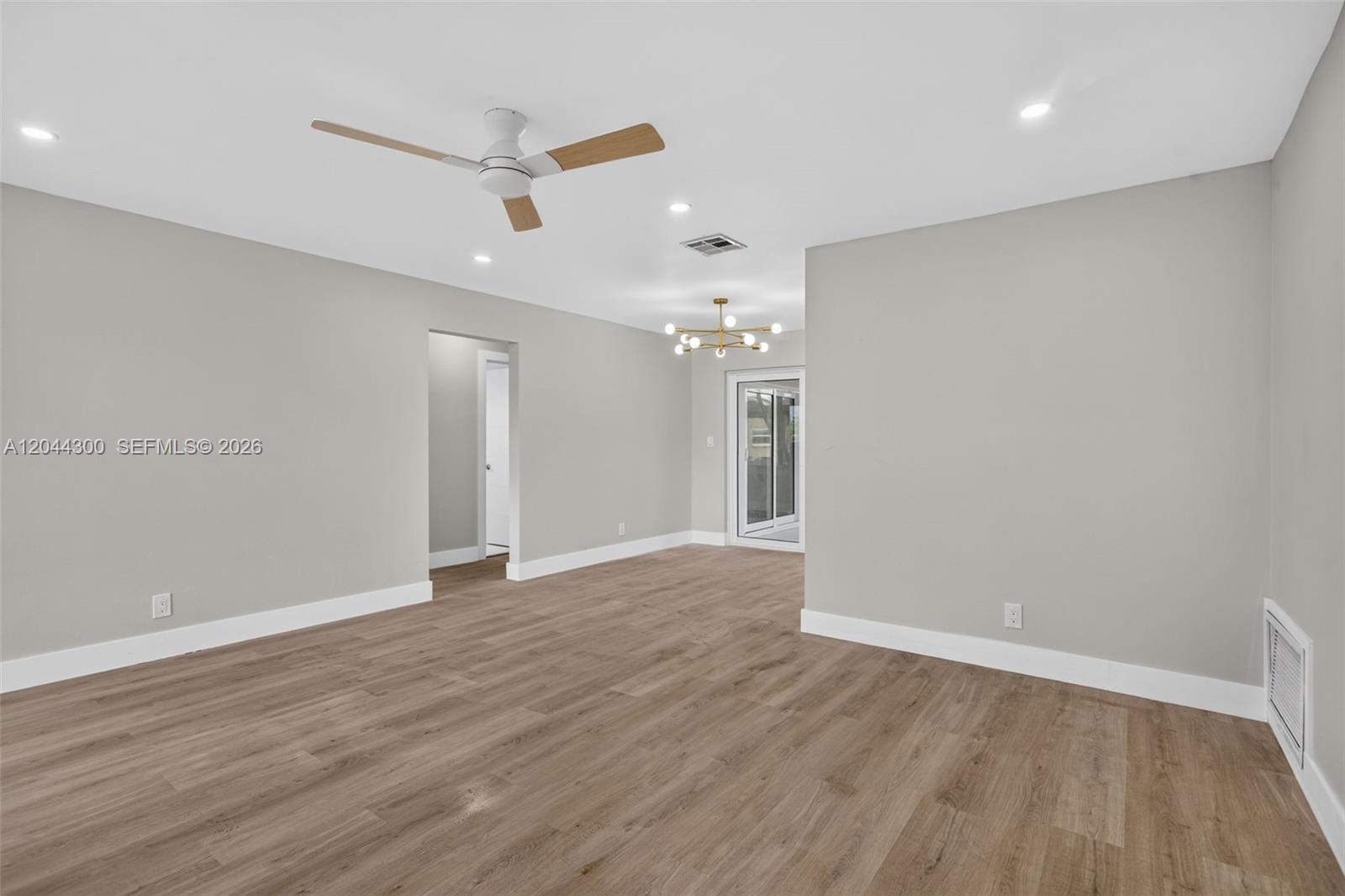 An empty room features light-colored walls, wood-look flooring, a ceiling fan, and a chandelier — 5711 NW 48th Ter, Tamarac FL 33319, TAMARAC, FL