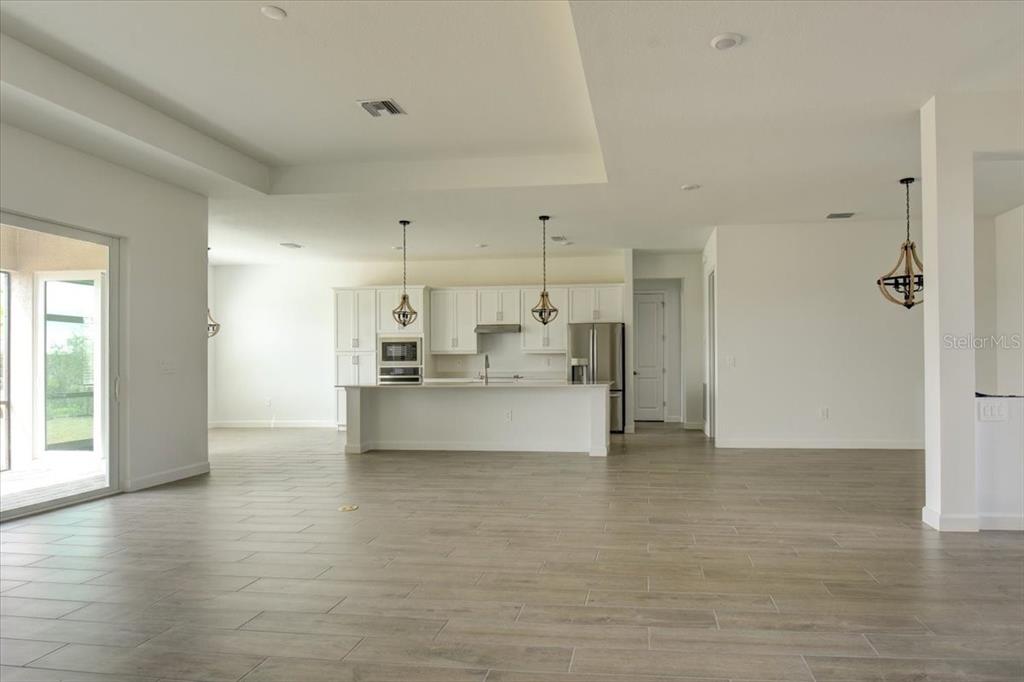 A bright, open-concept kitchen features white cabinetry, stainless steel appliances, and wood-look tile flooring — 7796 LAKES EDGE LANE, PORT CHARLOTTE, FL