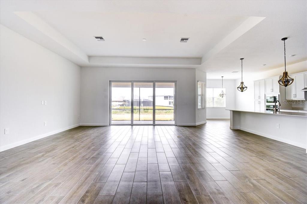 An open-concept living area with wood-look tile flooring, a tray ceiling, and a kitchen island — 7796 LAKES EDGE LANE, PORT CHARLOTTE, FL