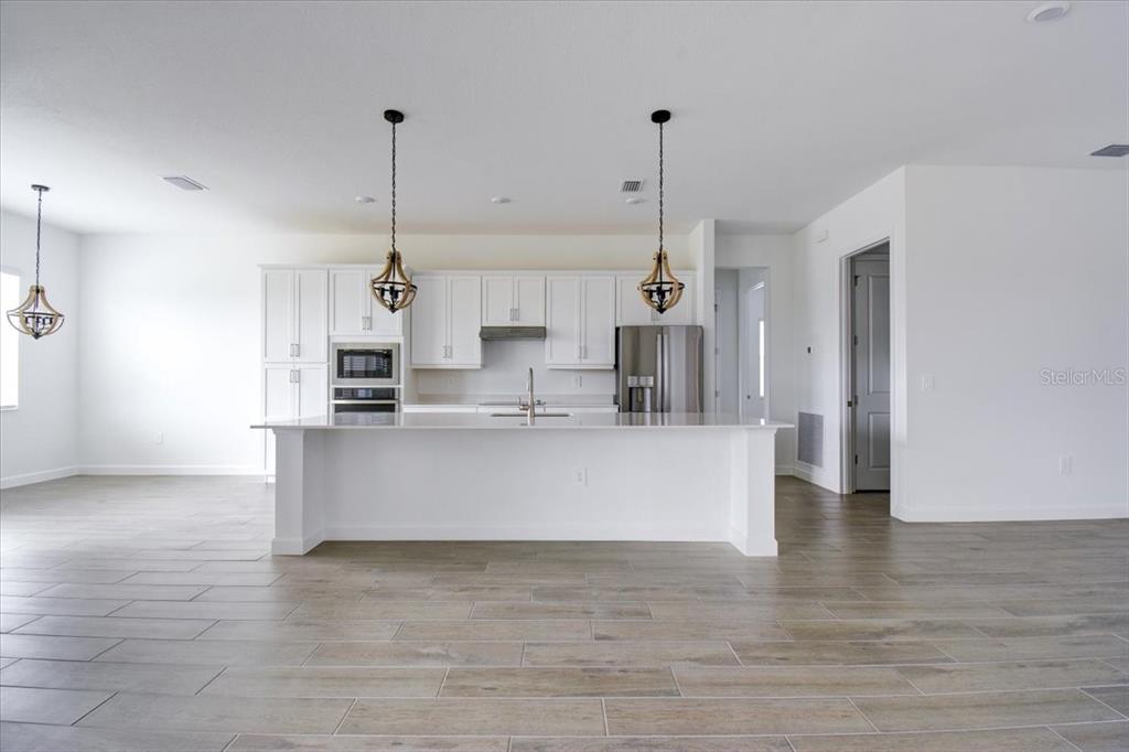 A modern kitchen features white cabinetry, a large island, stainless steel appliances, and wood-look flooring — 7796 LAKES EDGE LANE, PORT CHARLOTTE, FL