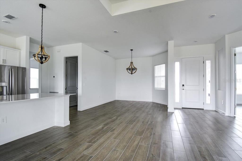 An open-concept dining and kitchen area features wood-look tile flooring and two rustic chandeliers — 7796 LAKES EDGE LANE, PORT CHARLOTTE, FL