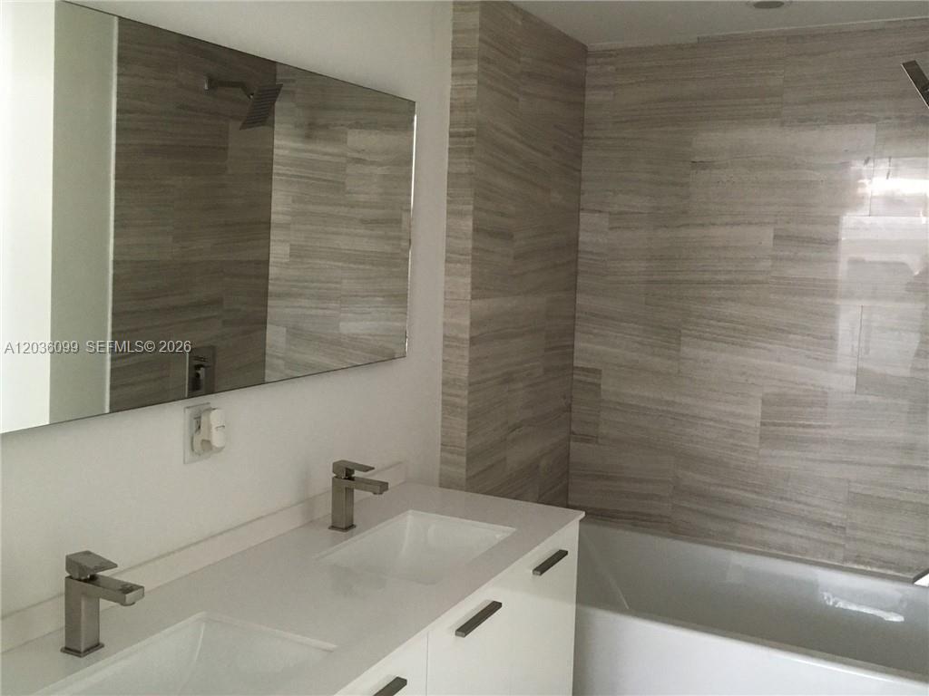 A modern bathroom features a double vanity, a glass-enclosed shower-tub combination, and tiled flooring — 1300 Brickell Bay Dr # 710, Miami FL 33131, MIAMI, FL