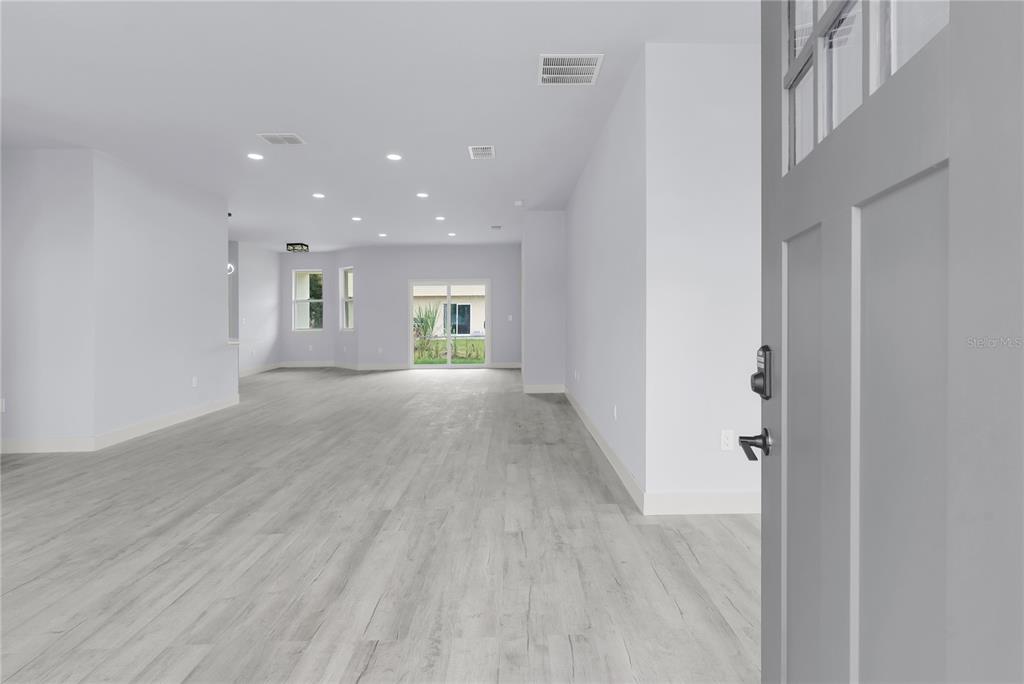 An open-concept living area features light wood-look flooring, recessed lighting, and sliding glass doors — 965 NANCY COURT, KISSIMMEE, FL