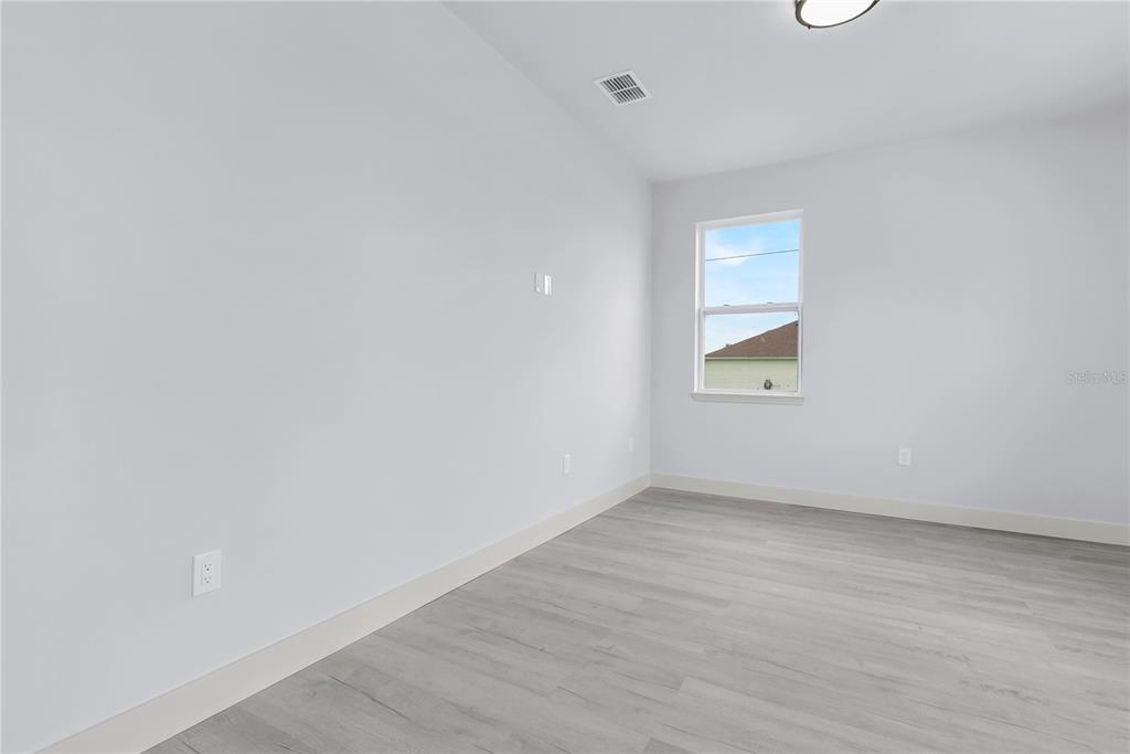 An empty room features light gray walls, wood-look flooring, a window, and white baseboards — 965 NANCY COURT, KISSIMMEE, FL