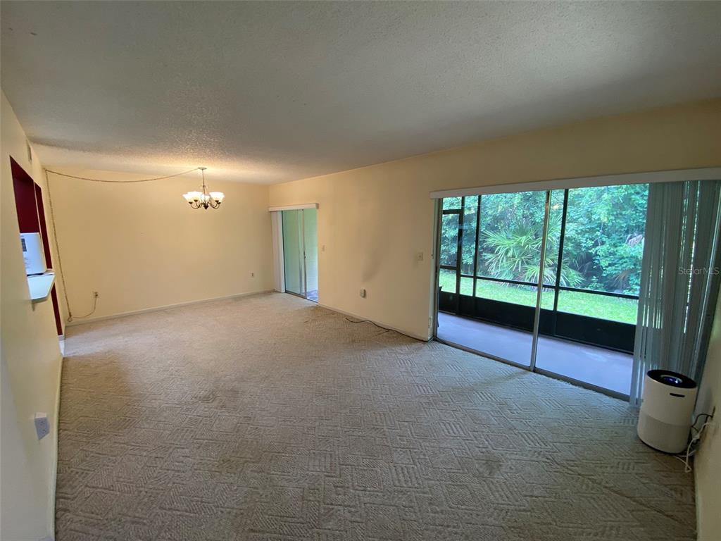 A carpeted living room features a sliding glass door leading to a screened-in porch — 160 LIVE OAK WOODS COURT UNIT 3A, DELTONA, FL