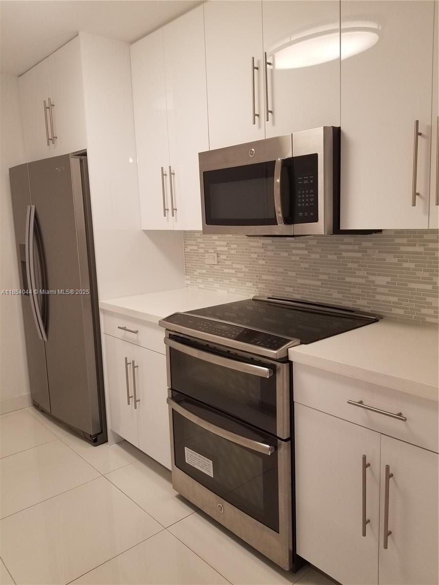 A modern kitchen features white cabinets, stainless steel appliances, and a light-colored tiled backsplash — 2651 NE 212th Ter # 103, Miami FL 33180, MIAMI, FL