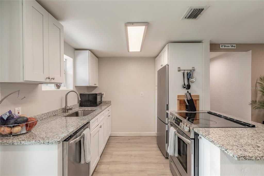 A galley kitchen features white cabinets, granite countertops, stainless steel appliances, and light wood flooring — 1245 ESSEX ROAD, DAYTONA BEACH, FL