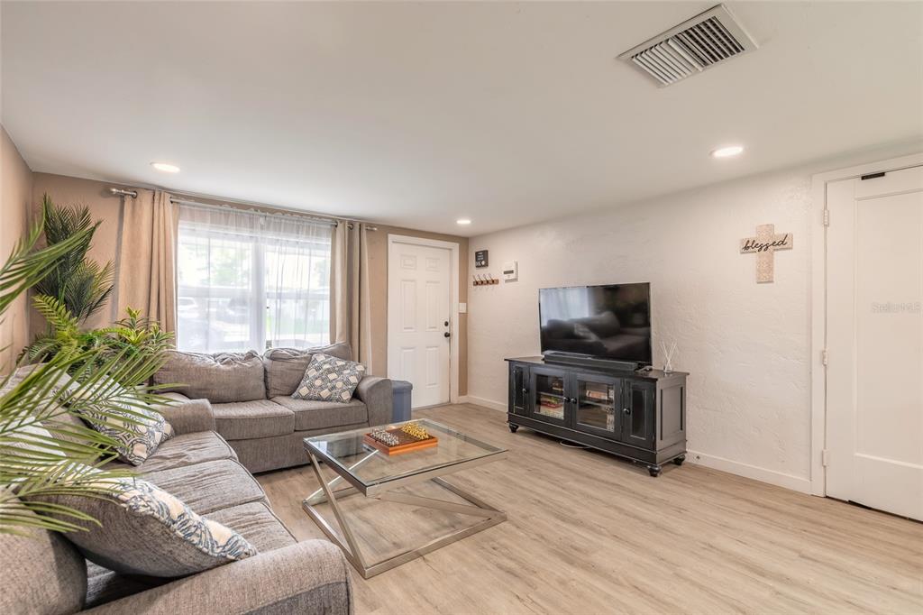 A living room features a gray sofa, glass coffee table, television console, and light wood flooring — 1245 ESSEX ROAD, DAYTONA BEACH, FL