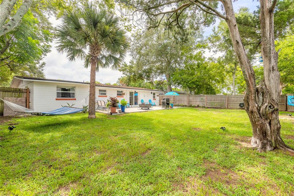 A backyard features a white house, a patio, a hammock, and several large trees — 1245 ESSEX ROAD, DAYTONA BEACH, FL