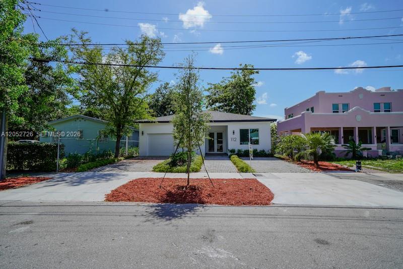 A single-story white house with a paved driveway sits between a green house and a pink building — 112 NW 24th Ct, Miami FL 33125, MIAMI, FL