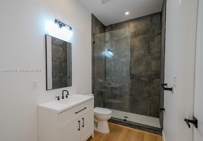 A bathroom features a white vanity, a glass-enclosed shower with dark tiles, and wood flooring — 112 NW 24th Ct, Miami FL 33125, MIAMI, FL