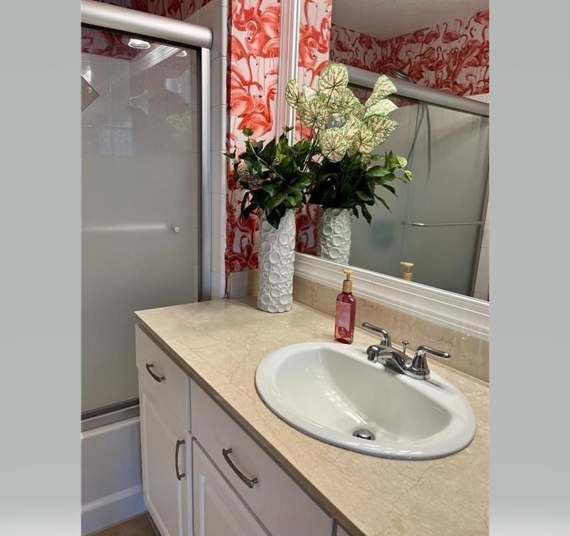 A bathroom vanity with a beige countertop, white cabinets, and flamingo-patterned wallpaper — 275 Murcia Drive # 308, Jupiter FL 33458, JUPITER, FL