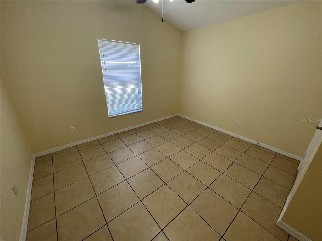 An empty bedroom features beige walls, a single window with blinds, and tan tile flooring — 1406 VISTA DEL LAGO BOULEVARD, DUNDEE, FL