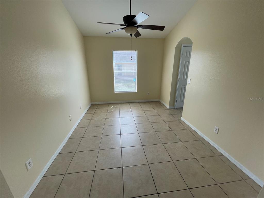 An empty room features beige walls, large square floor tiles, a ceiling fan, and a window — 1406 VISTA DEL LAGO BOULEVARD, DUNDEE, FL