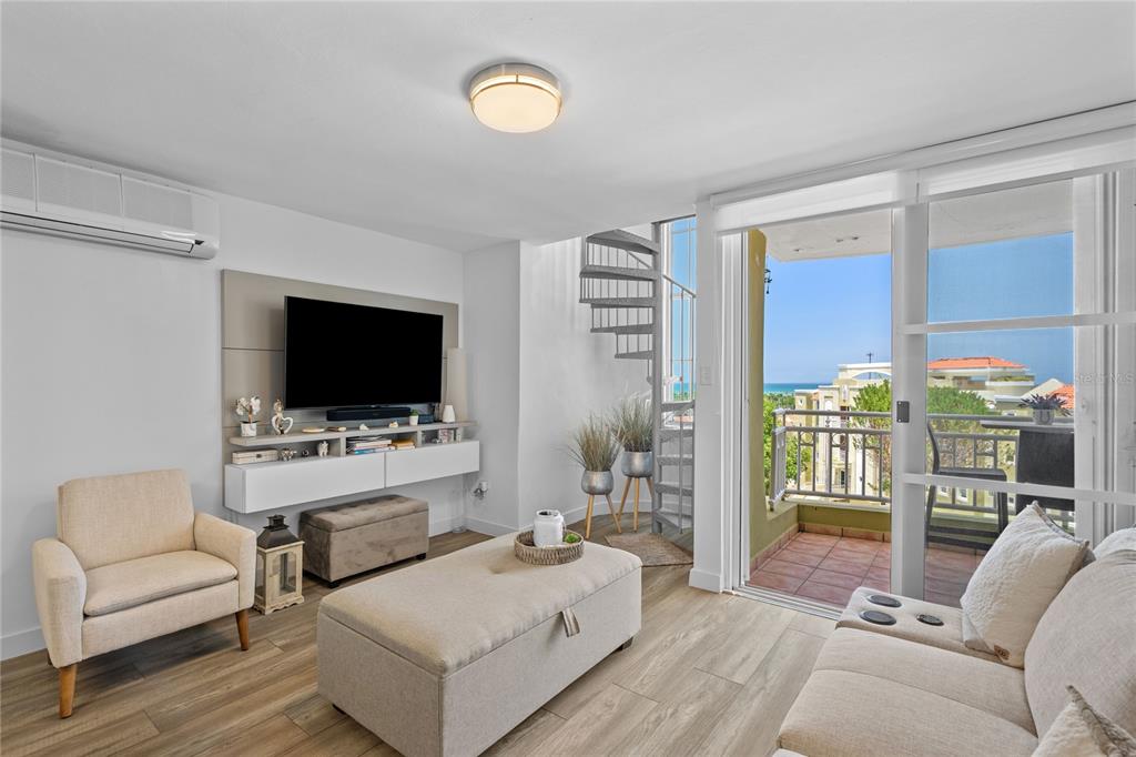 A living room with a spiral staircase, wall-mounted television, and a balcony overlooking the ocean — Castillos Del Mar LAURO PIÑERO UNIT KC-PH, CEIBA, PR