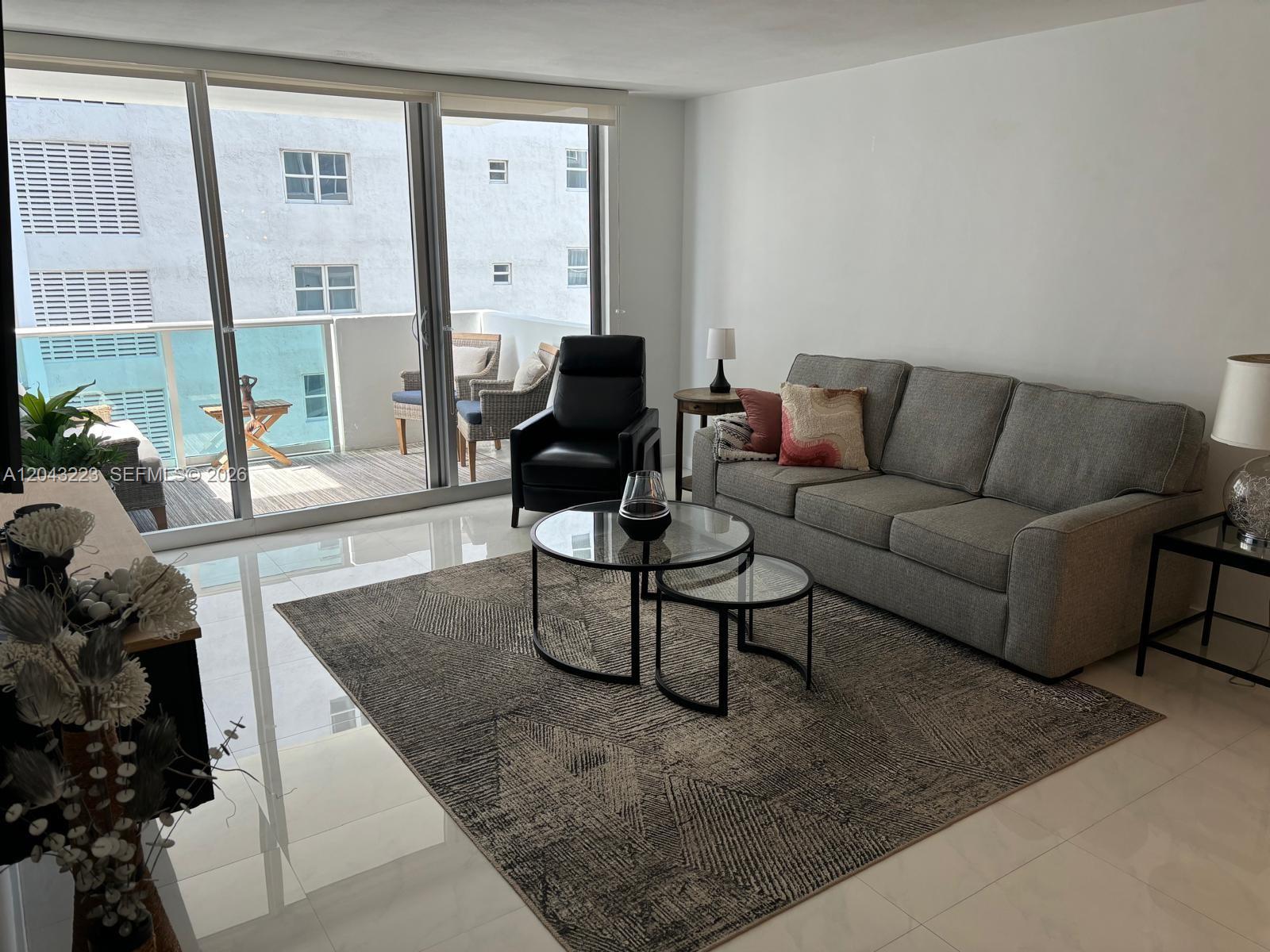 A modern living room features a wall-mounted television, a neutral sofa, and a glass balcony door — 1200 West Ave # 720, Miami Beach FL 33139, MIAMI BEACH, FL