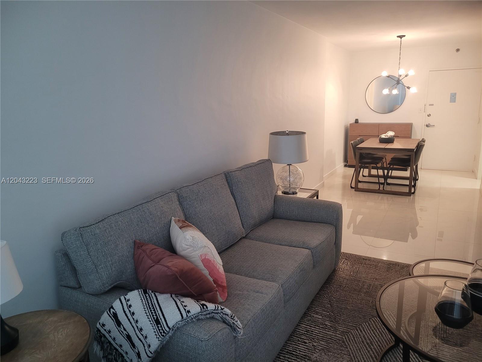 A living room features a gray sofa, glass coffee tables, and a balcony with outdoor seating — 1200 West Ave # 720, Miami Beach FL 33139, MIAMI BEACH, FL
