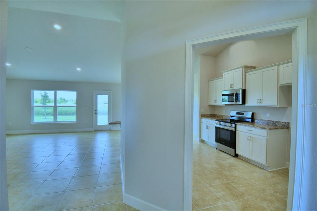 A view from a hallway looking into a kitchen with white cabinets and tiled floors — 4433 JUNEBERRY DRIVE, AUBURNDALE, FL