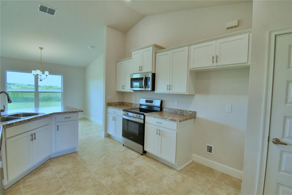 A kitchen features white cabinets, granite countertops, stainless steel appliances, and tile flooring — 4433 JUNEBERRY DRIVE, AUBURNDALE, FL
