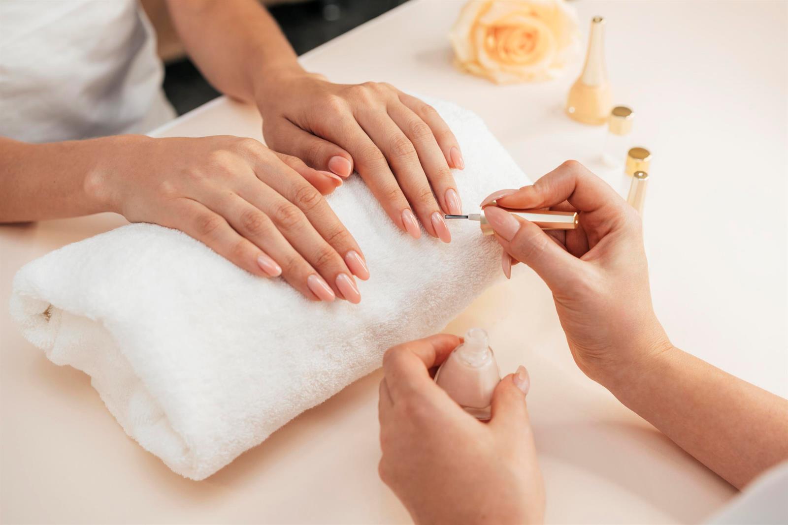 A manicurist applies light pink nail polish to a client's fingernails resting on a white towel — 1 Nail Salon, North Miami FL, NORTH MIAMI, FL