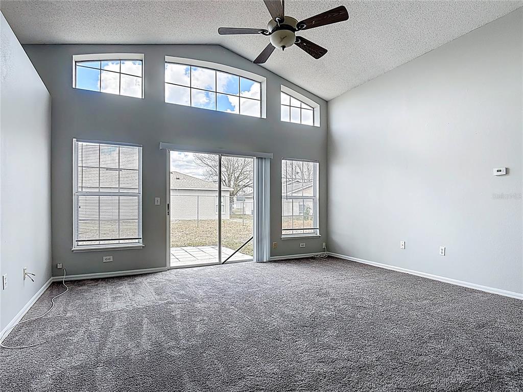 A living room with gray carpet, vaulted ceilings, a ceiling fan, and sliding glass doors — 40 COVENTRY COURT, KISSIMMEE, FL