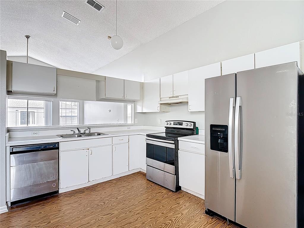 A kitchen features white cabinets, stainless steel appliances, and wood-look flooring under a vaulted ceiling — 40 COVENTRY COURT, KISSIMMEE, FL