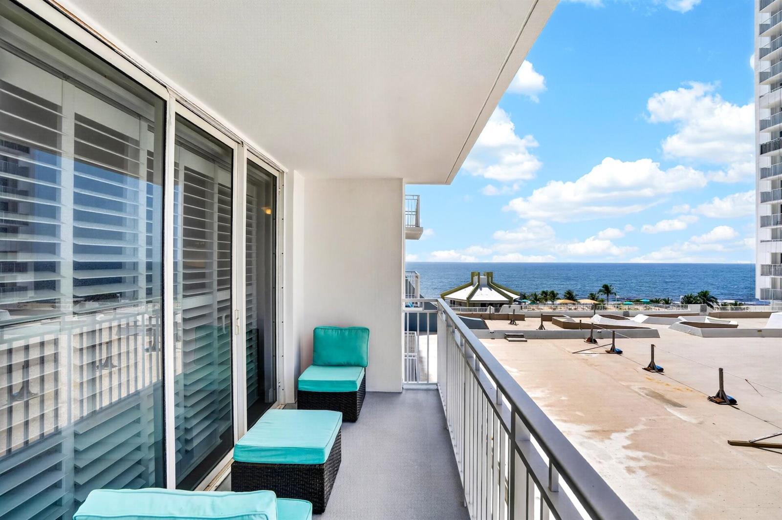 A balcony with turquoise cushioned chairs overlooks a flat roof and the ocean beyond — 101 Briny Avenue # 808, Pompano Beach FL 33062, POMPANO BEACH, FL