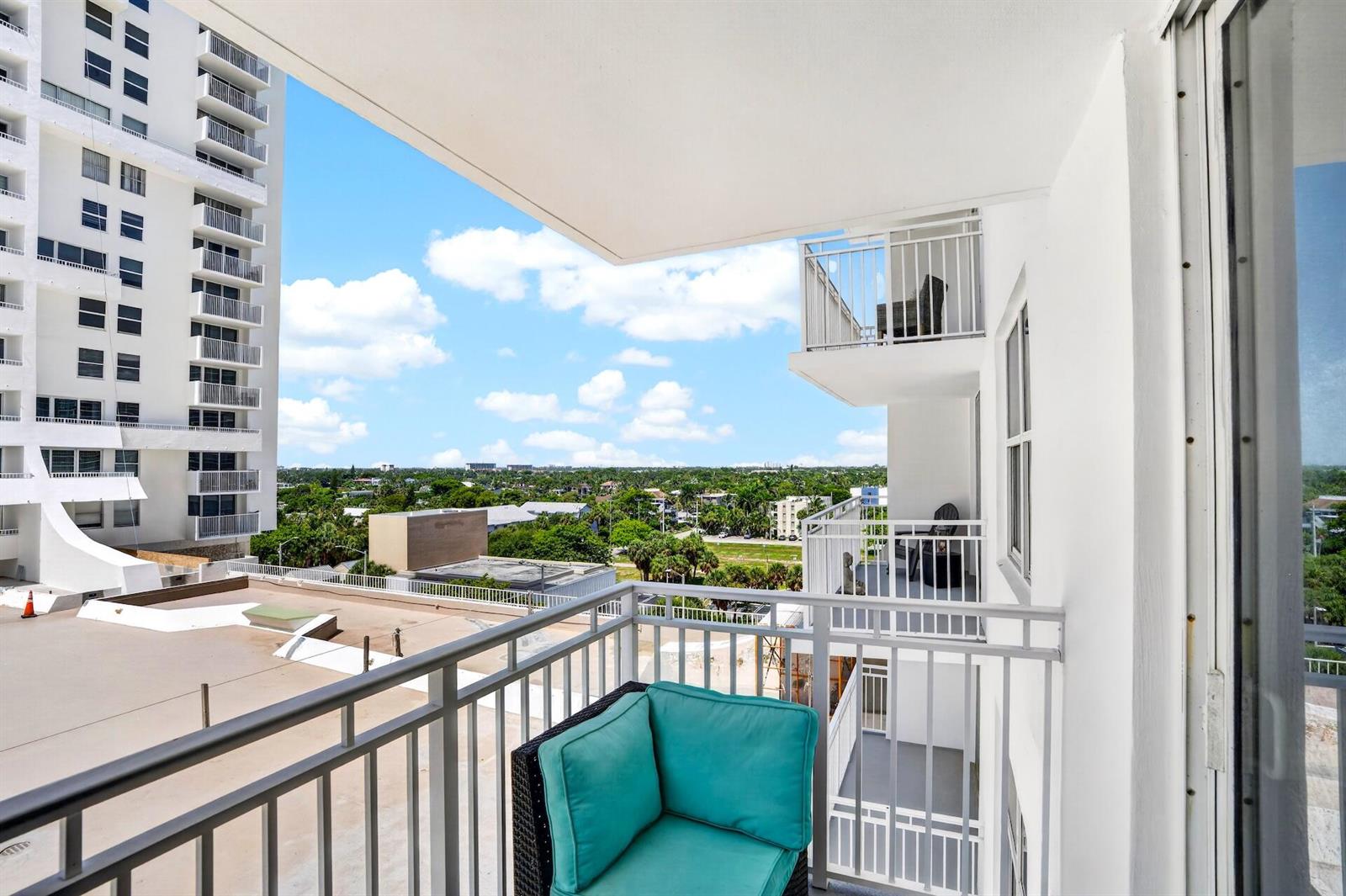 A balcony with a teal corner chair overlooks a neighboring building and a green landscape — 101 Briny Avenue # 808, Pompano Beach FL 33062, POMPANO BEACH, FL