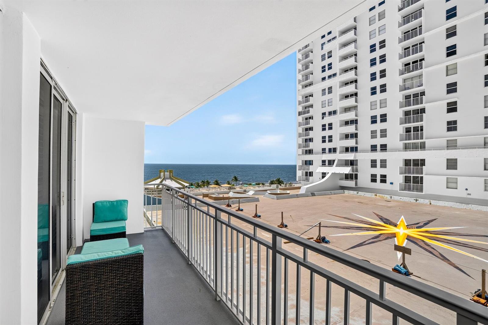 A balcony with outdoor seating overlooks a large flat roof and the ocean beyond — 101 Briny Avenue # 808, Pompano Beach FL 33062, POMPANO BEACH, FL