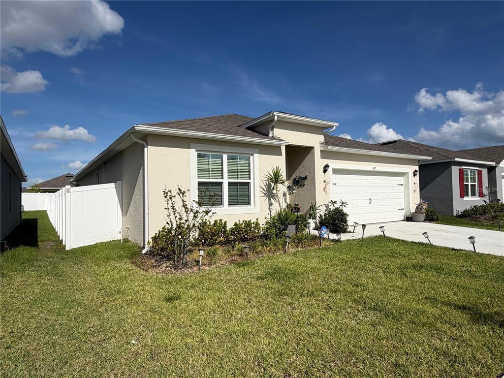 A single-story suburban house with a white garage, beige stucco exterior, and a white fence — 1677 THREE BARS ROAD, KISSIMMEE, FL