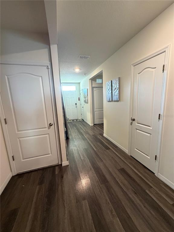 A hallway with wood-look flooring leads toward a front door with two side doors — 1677 THREE BARS ROAD, KISSIMMEE, FL