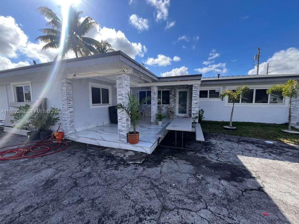 A house exterior features a tiled patio, stone-clad columns, and a cracked asphalt driveway — 19700 NW 6th Pl, Miami Gardens FL 33169, MIAMI GARDENS, FL