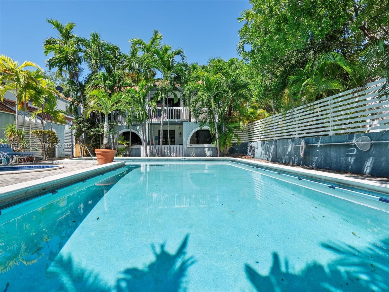 A rectangular swimming pool sits in a backyard with palm trees and a white fence — 515 NE 38th St # 10, Miami FL 33137, MIAMI, FL