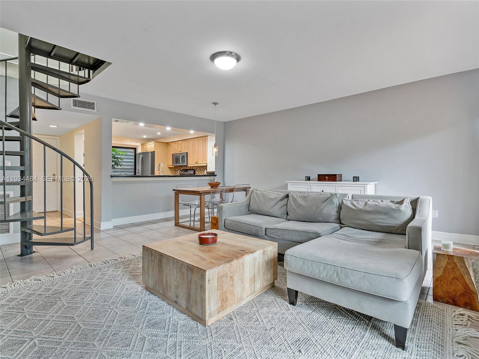 A living room features a spiral staircase, a sectional sofa, and an open kitchen pass-through — 515 NE 38th St # 10, Miami FL 33137, MIAMI, FL