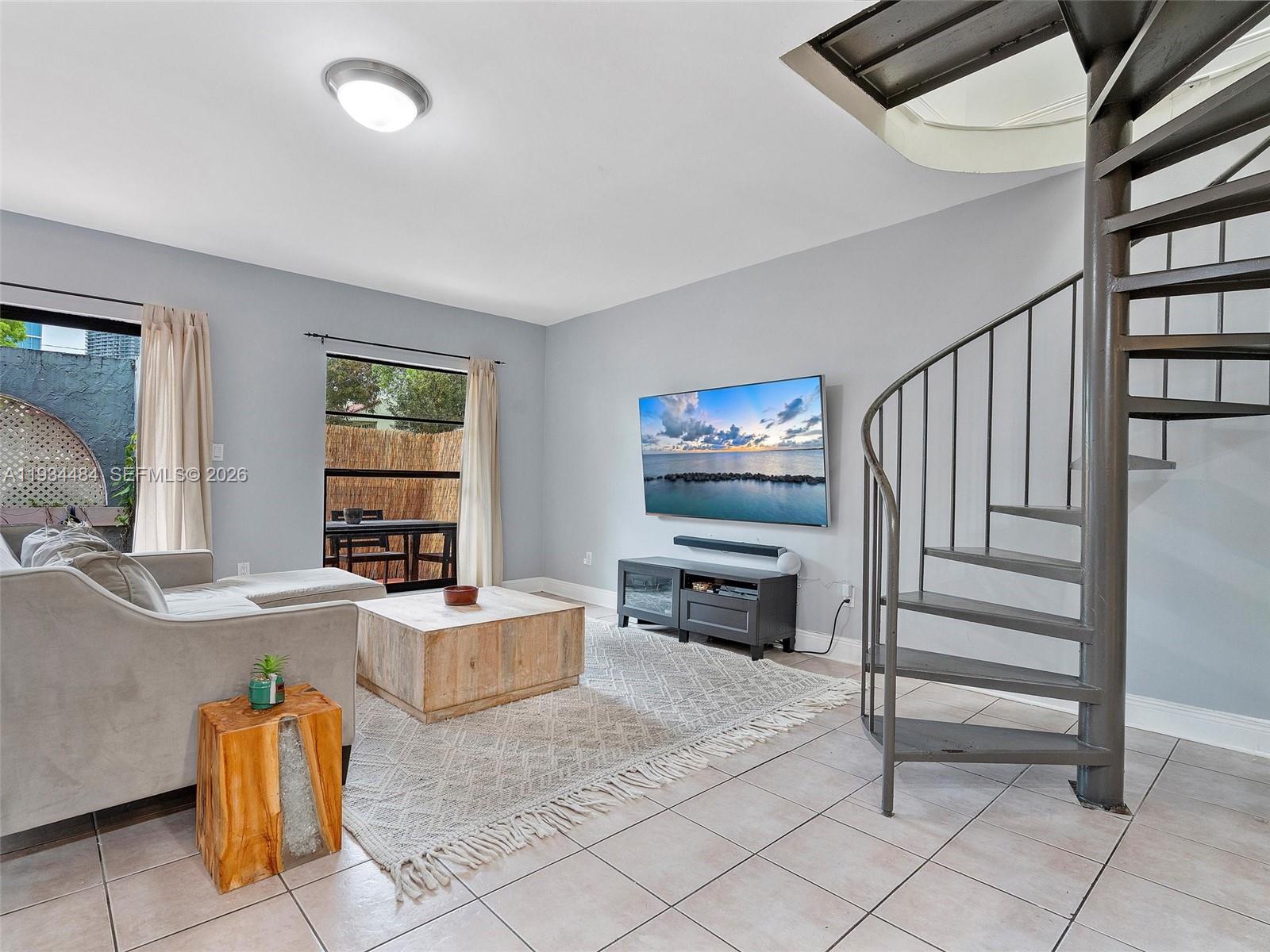 A living room features a spiral staircase, a wall-mounted television, and tile flooring — 515 NE 38th St # 10, Miami FL 33137, MIAMI, FL