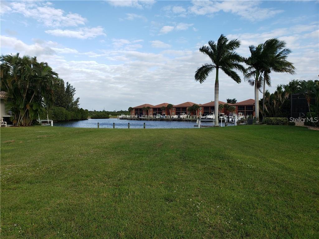 A grassy lawn overlooks a canal with docked boats and multi-story residential buildings — 3524 TERIN COURT, PUNTA GORDA, FL