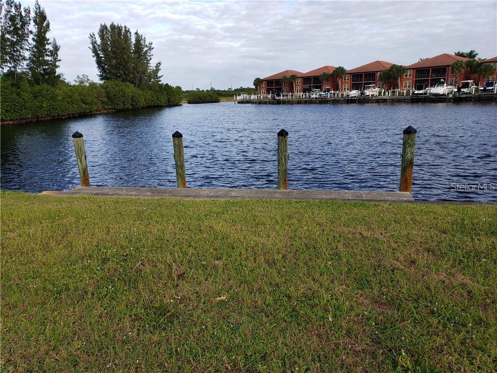 A grassy lawn overlooks a canal with four wooden pilings and a distant apartment complex — 3524 TERIN COURT, PUNTA GORDA, FL