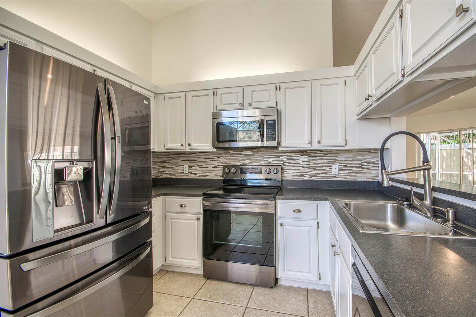 A kitchen with white cabinets, stainless steel appliances, dark countertops, and a tiled backsplash — 252 Moccasin Trail W, Jupiter FL 33458, JUPITER, FL
