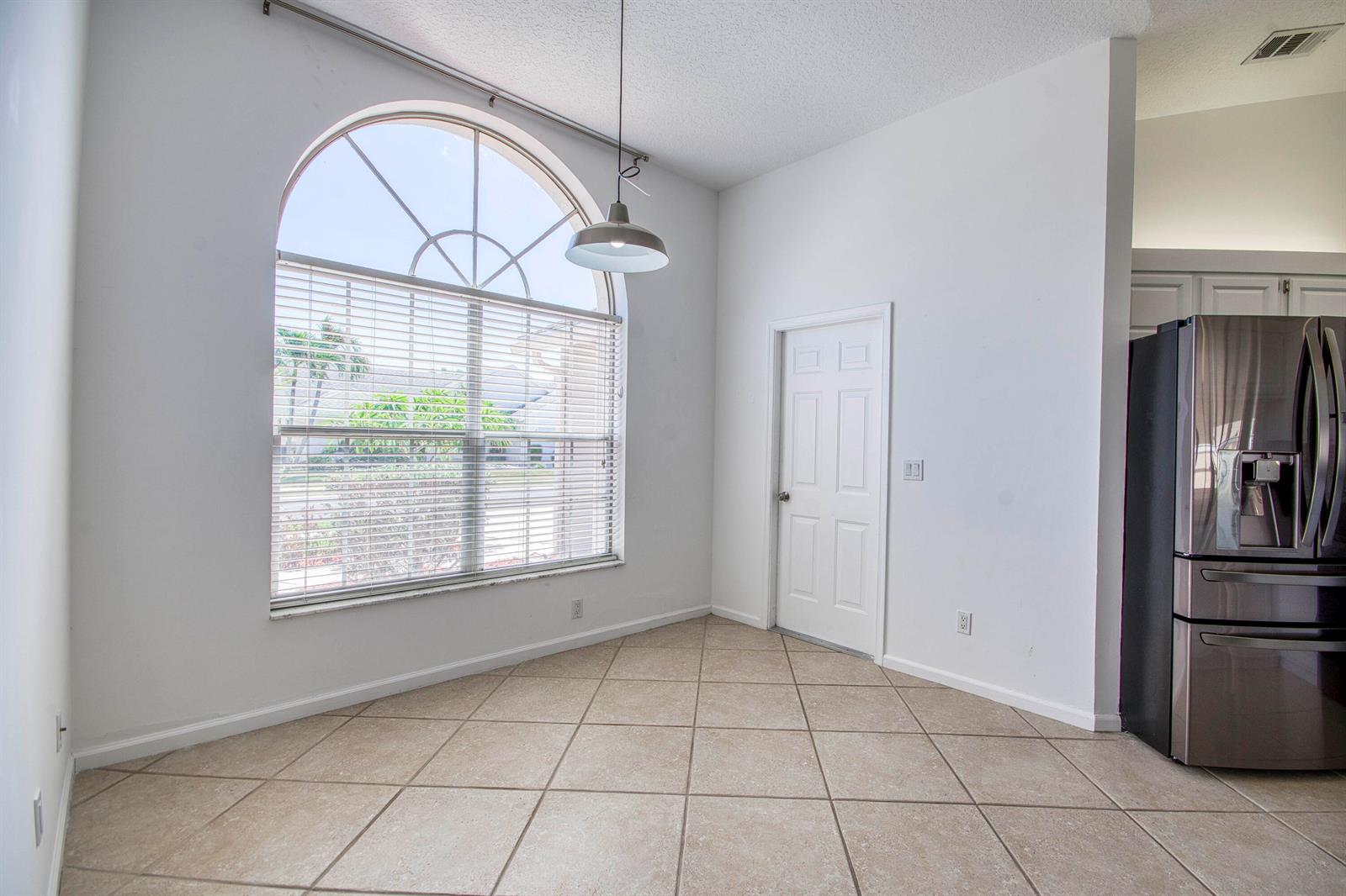 A dining area features a large arched window, tile flooring, and a stainless steel refrigerator — 252 Moccasin Trail W, Jupiter FL 33458, JUPITER, FL