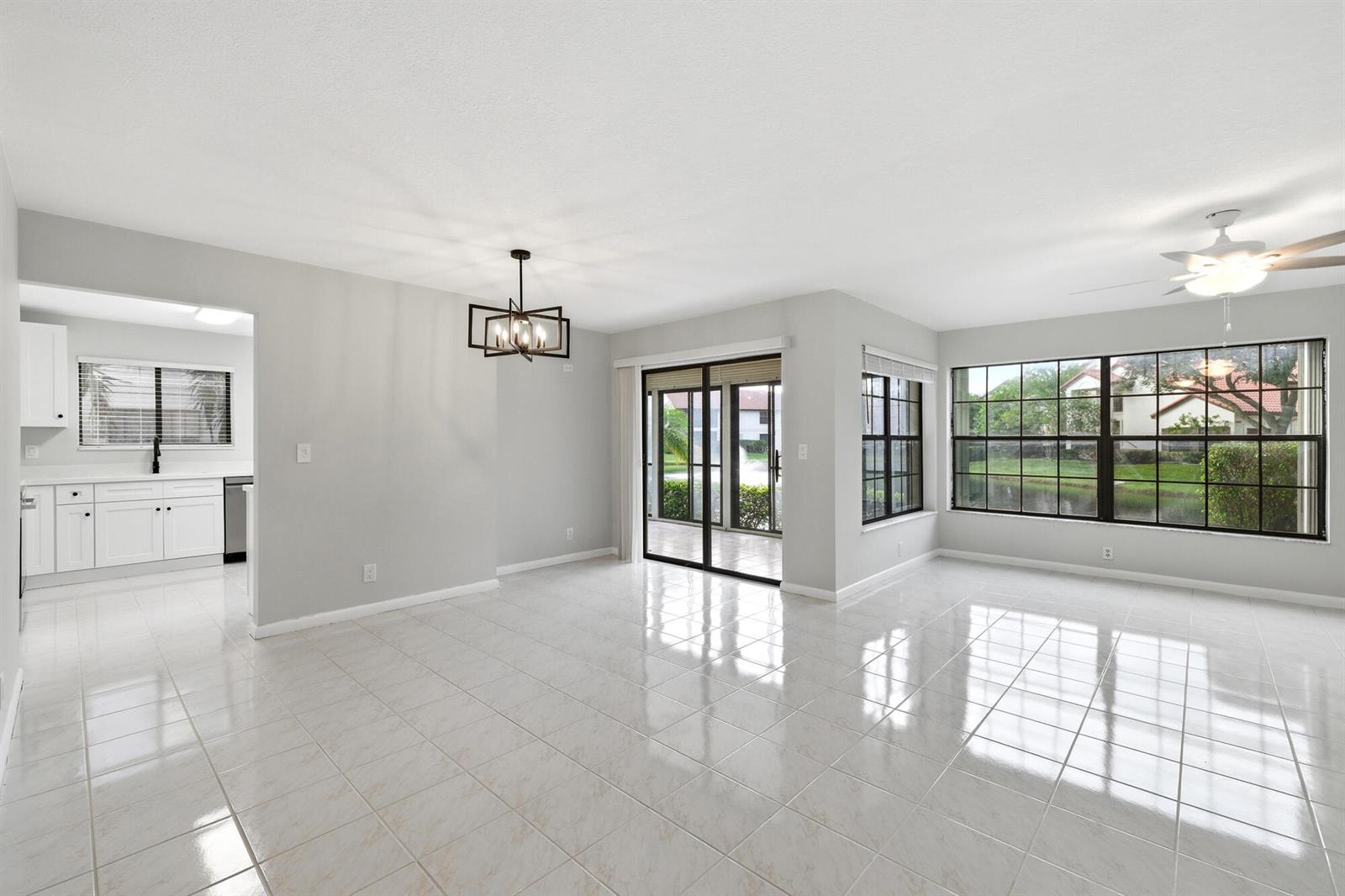 An open-concept dining and living area features light tile flooring, a chandelier, and large windows — 3357 Jog Park Drive # 4212c, FL 33467, FL
