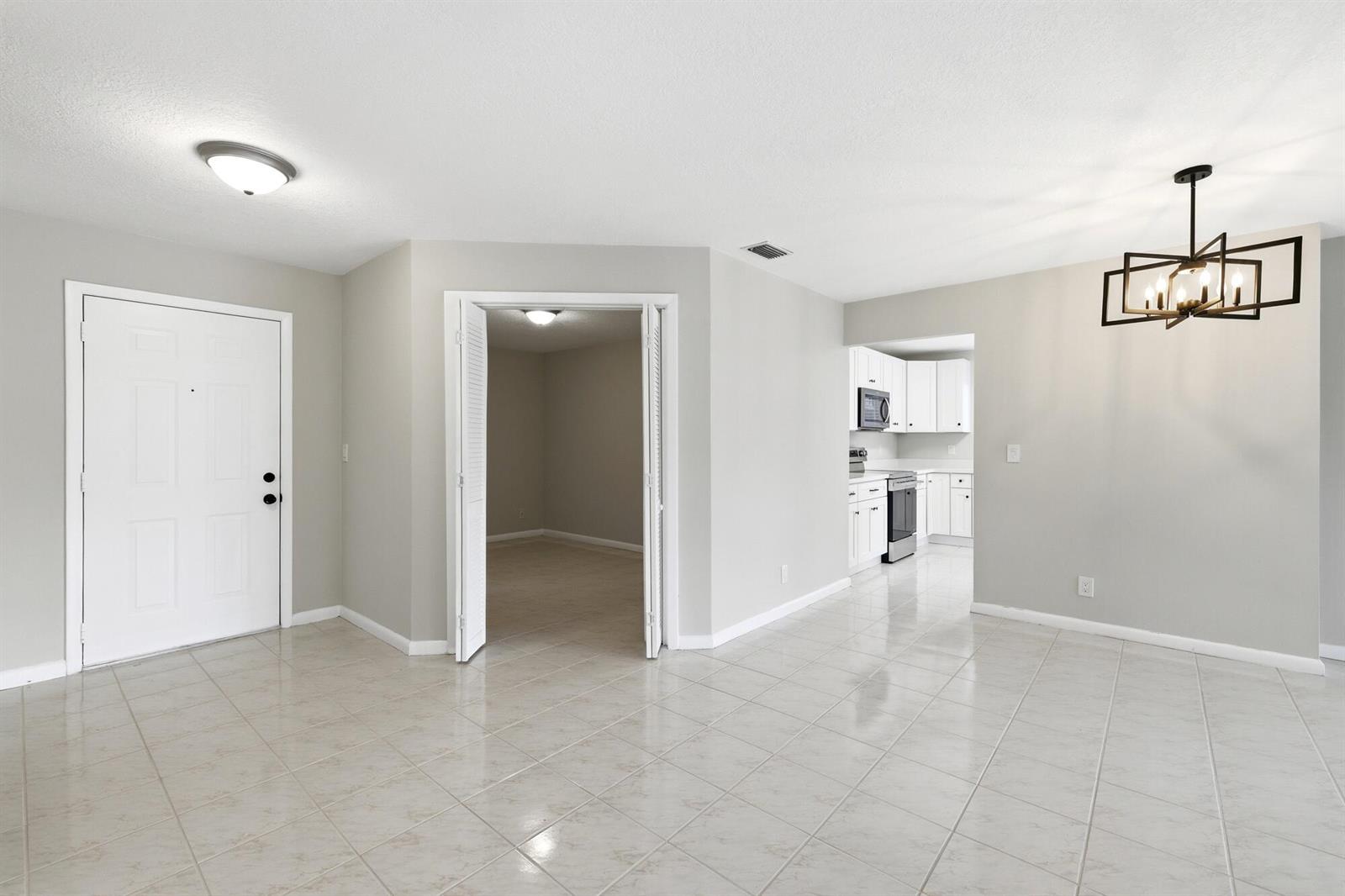 A living area with tile floors, a white front door, and an open kitchen view — 3357 Jog Park Drive # 4212c, FL 33467, FL