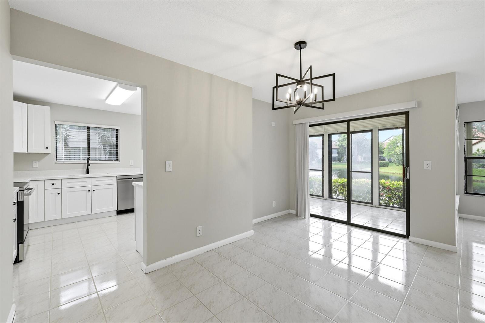A dining area with tile floors and a modern chandelier opens to a screened patio — 3357 Jog Park Drive # 4212c, FL 33467, FL